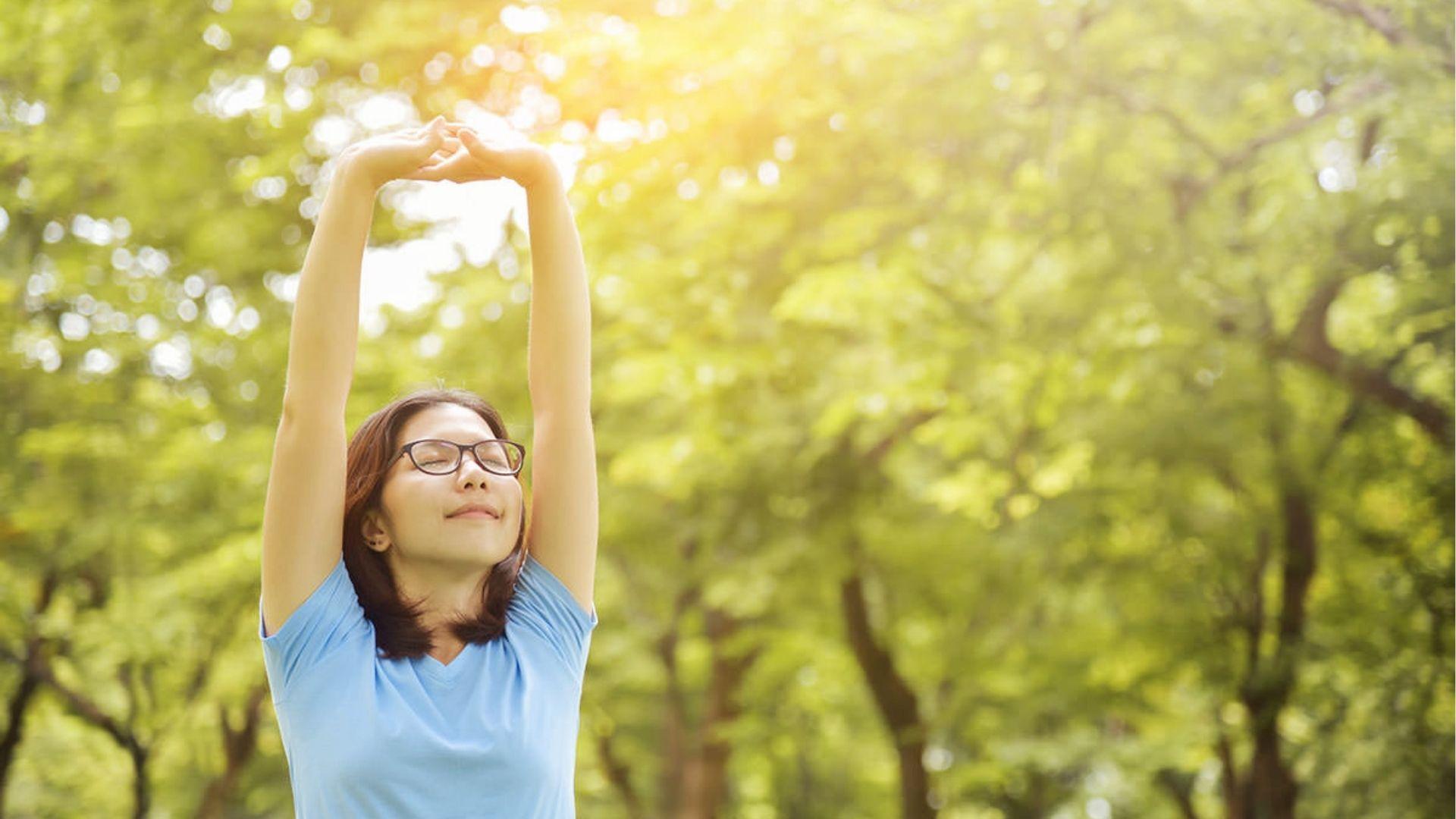 Calm woman stretching in sunlight, representing hangxiety recovery through fresh air and exercise