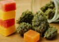 Stack of red and yellow cannabis gummies next to cannabis flower buds on wooden table surface