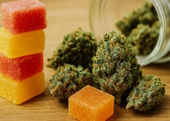 Stack of red and yellow cannabis gummies next to cannabis flower buds on wooden table surface