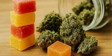 Stack of red and yellow cannabis gummies next to cannabis flower buds on wooden table surface