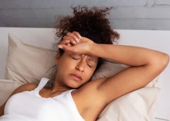Woman lying awake in bed with hand on forehead, showing insomnia and stress from hangxiety lasting hours
