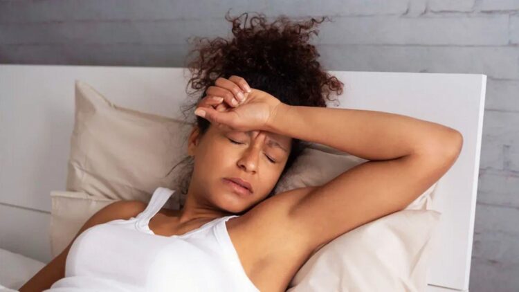 Woman lying awake in bed with hand on forehead, showing insomnia and stress from hangxiety lasting hours