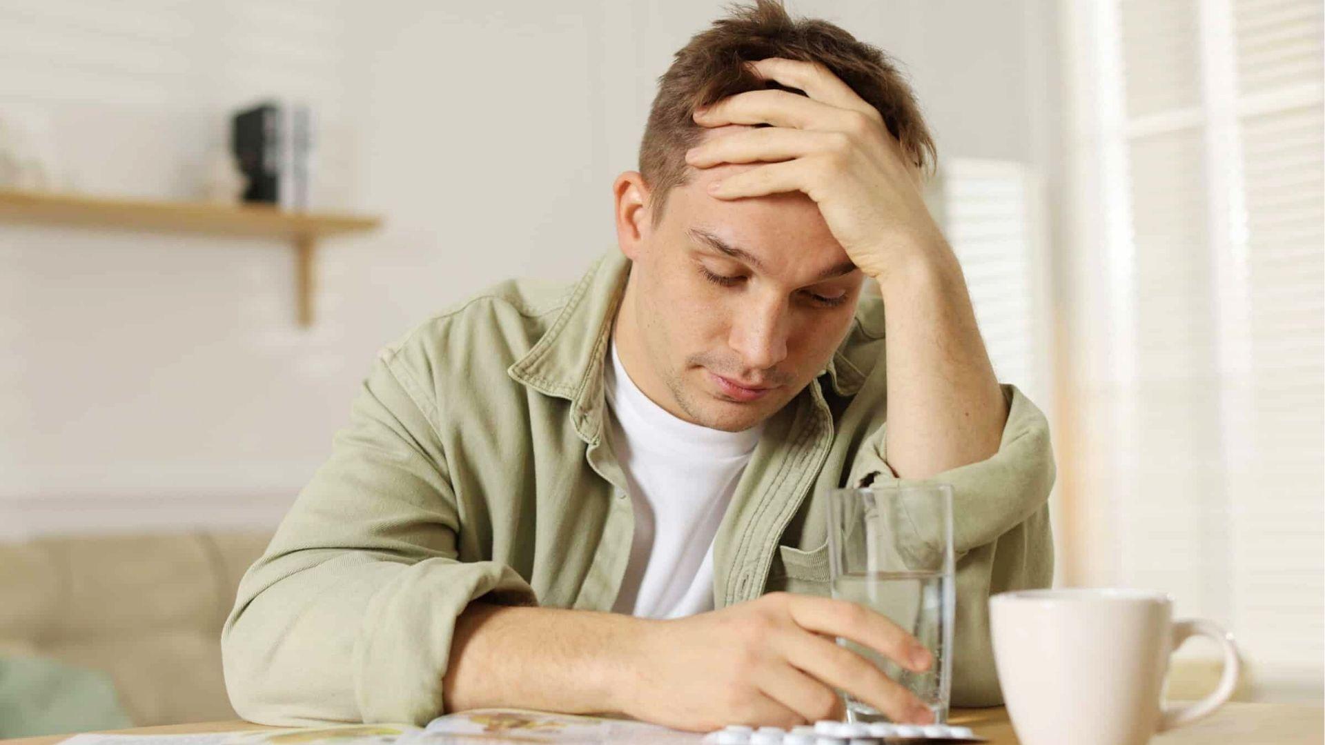 Anxious young man holding his head at table with water, showing common hangxiety symptoms like worry and headache