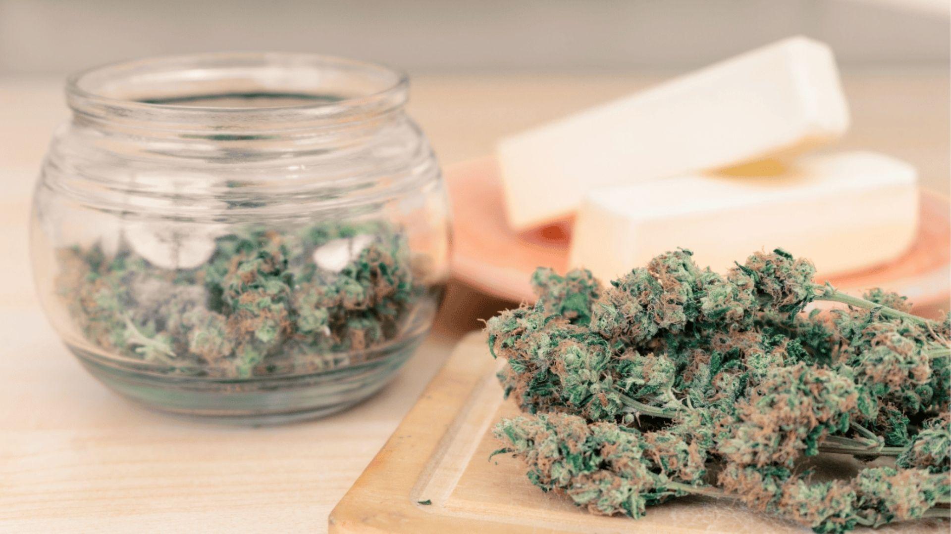 Dried cannabis buds and jar next to butter sticks for making homemade cannabutter for cooking recipes