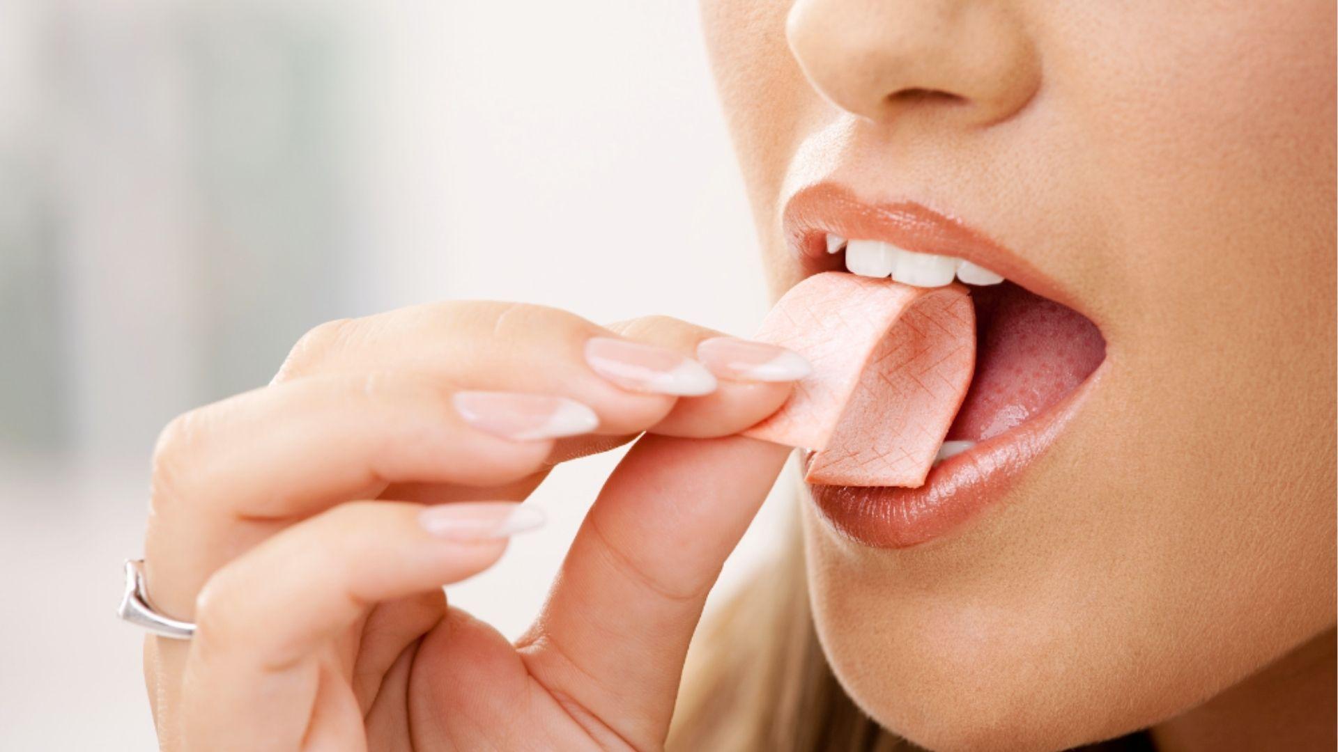 Woman placing pink chewing gum on tongue to increase saliva flow and combat dry mouth symptoms from cannabis edibles