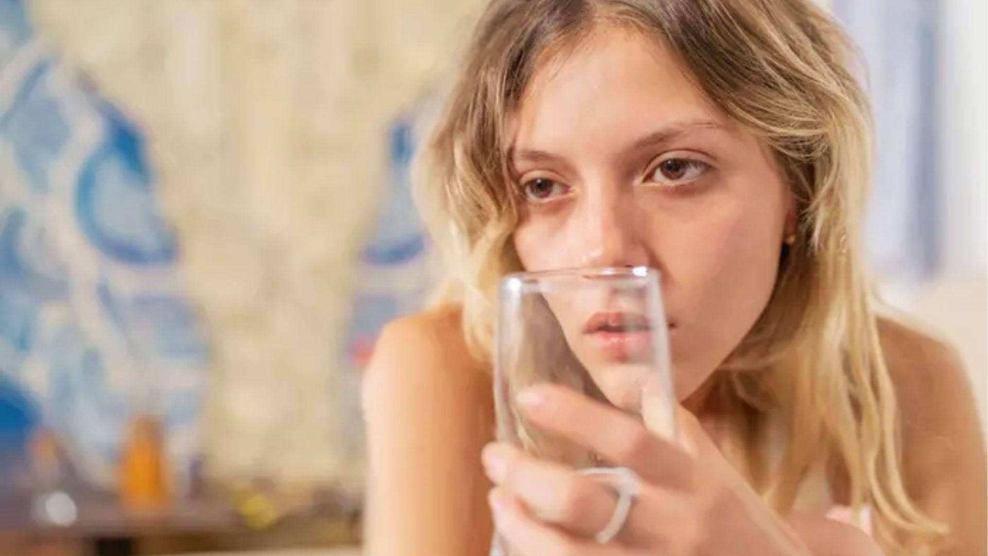 Tired woman holding glass of water in morning, representing dehydration and mental fog linked to hangxiety