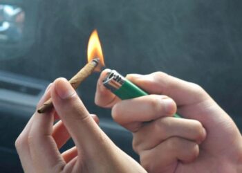 Lighting a rolled cannabis joint with a green lighter inside car before removing weed smell naturally