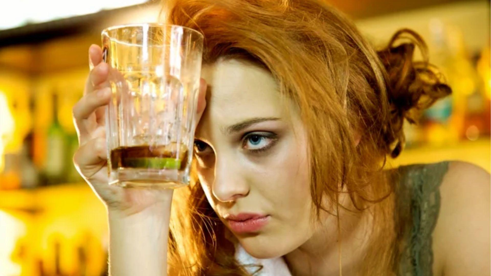 Stressed woman with messy hair holding glass to head, illustrating regret and anxiety during hangxiety after drinking