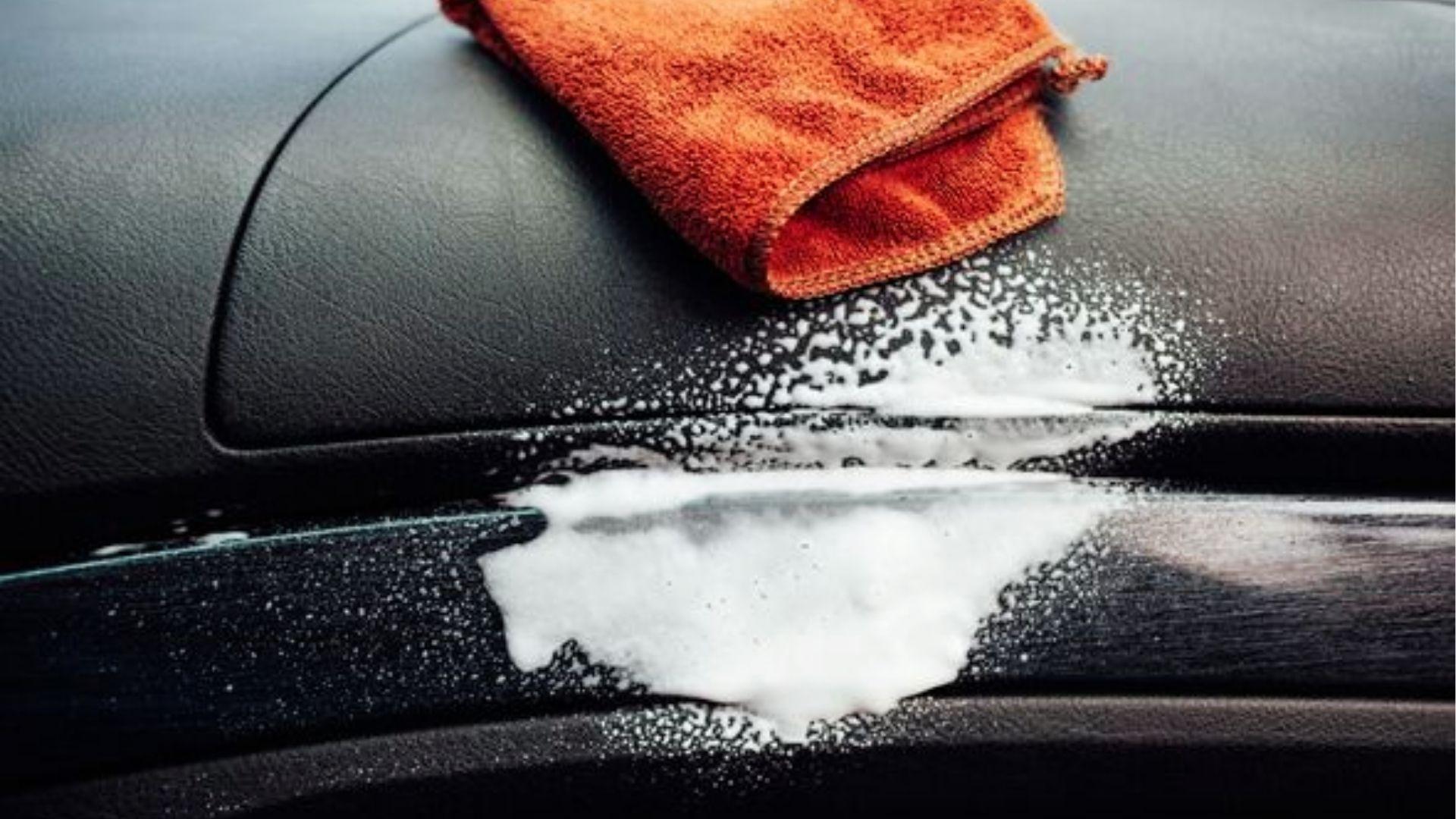 Using orange microfiber cloth and foam cleaner on car dashboard to remove weed odor naturally