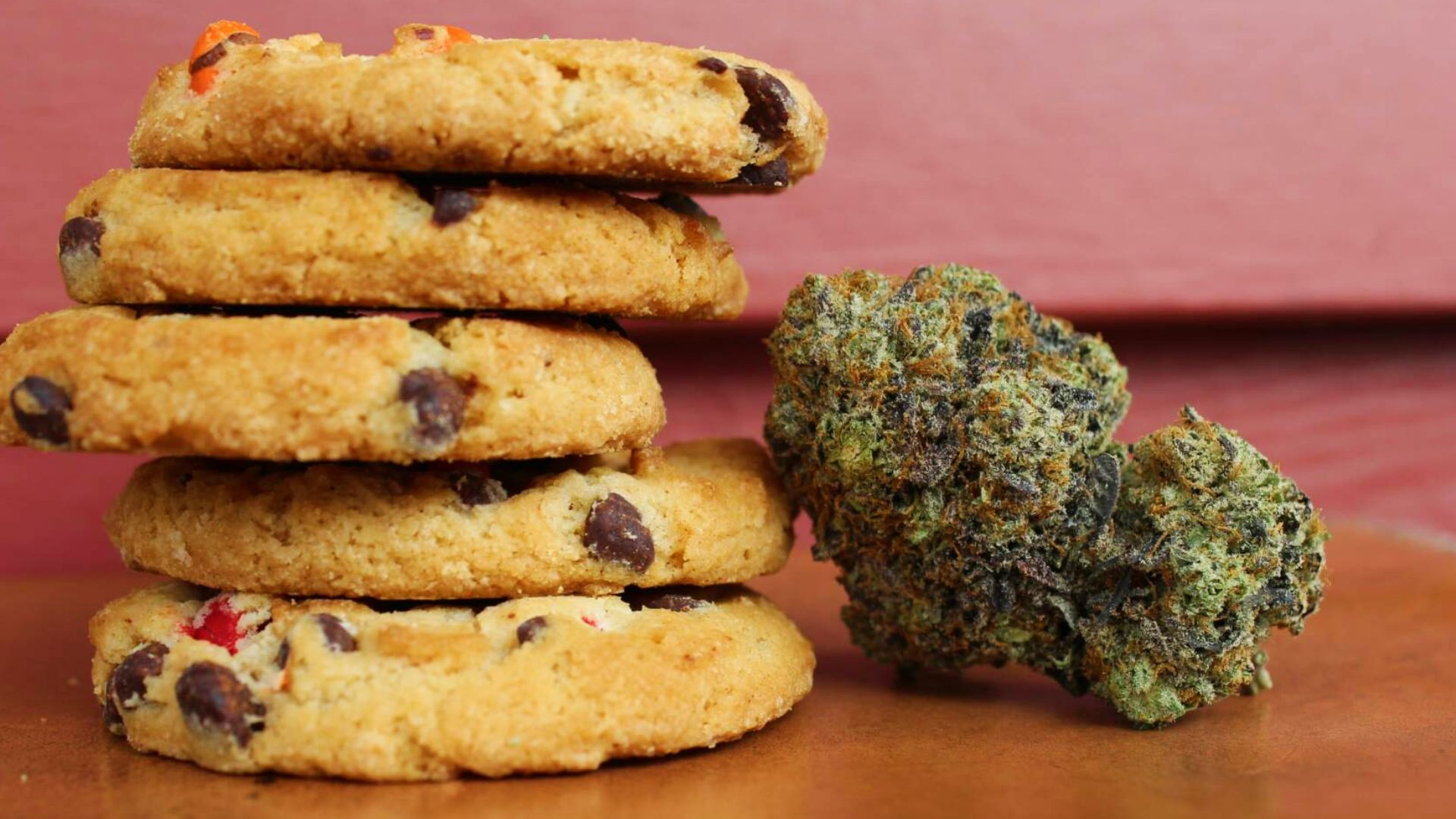 Stack of chocolate chip cannabis cookies next to dried buds on wooden surface for simple homemade edibles recipes