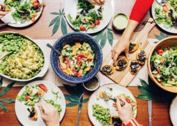 Friends sharing cannabis infused dinner with salads, pasta, and bruschetta on wood table for group edibles recipes