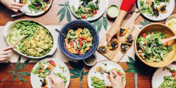 Friends sharing cannabis infused dinner with salads, pasta, and bruschetta on wood table for group edibles recipes