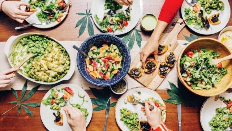 Friends sharing cannabis infused dinner with salads, pasta, and bruschetta on wood table for group edibles recipes