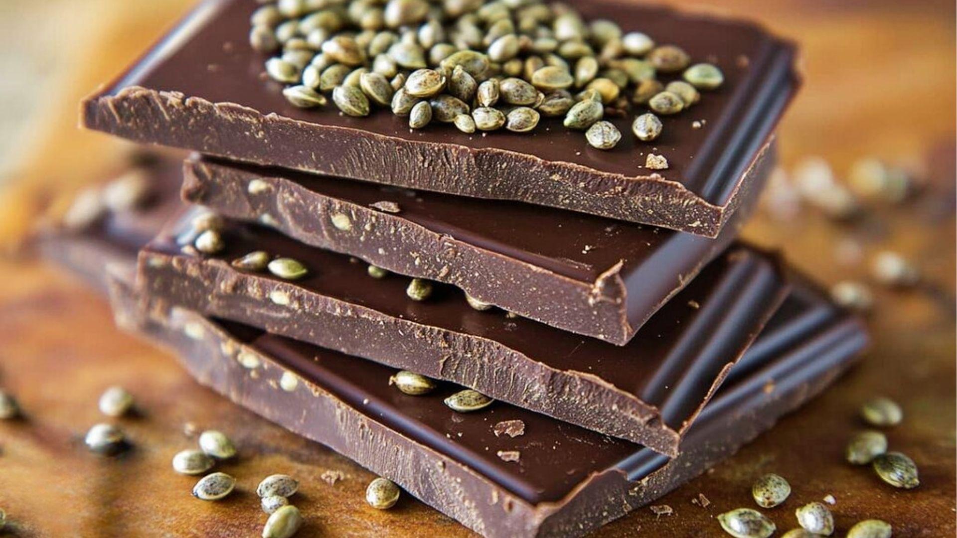 Stacked dark chocolate bars topped with hemp seeds on wooden table for cannabis infused chocolate recipes