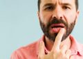 Bearded man in pink shirt pointing to dry lips and mouth discomfort caused by dehydration from cannabis edible consumption