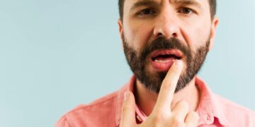 Bearded man in pink shirt pointing to dry lips and mouth discomfort caused by dehydration from cannabis edible consumption