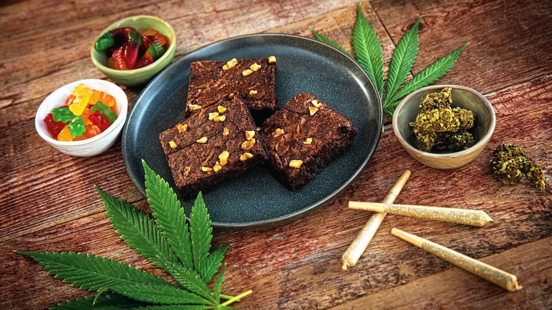 Cannabis edibles, joints, leaves, and buds on a wood table. Edibles expire per food label, often 3-6 months.