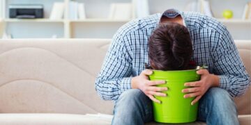 Man feeling nauseous and vomiting into green bucket as a common weed hangover side effect