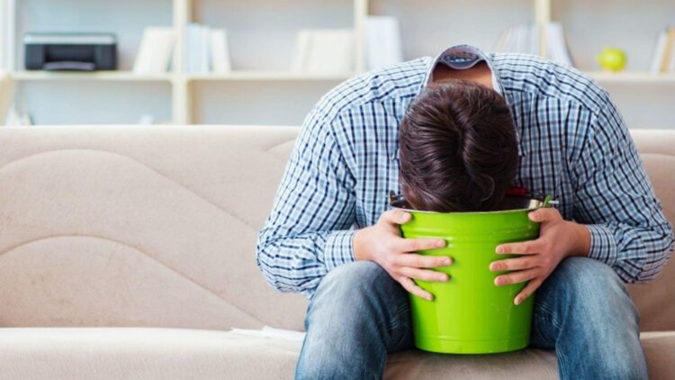 Man feeling nauseous and vomiting into green bucket as a common weed hangover side effect