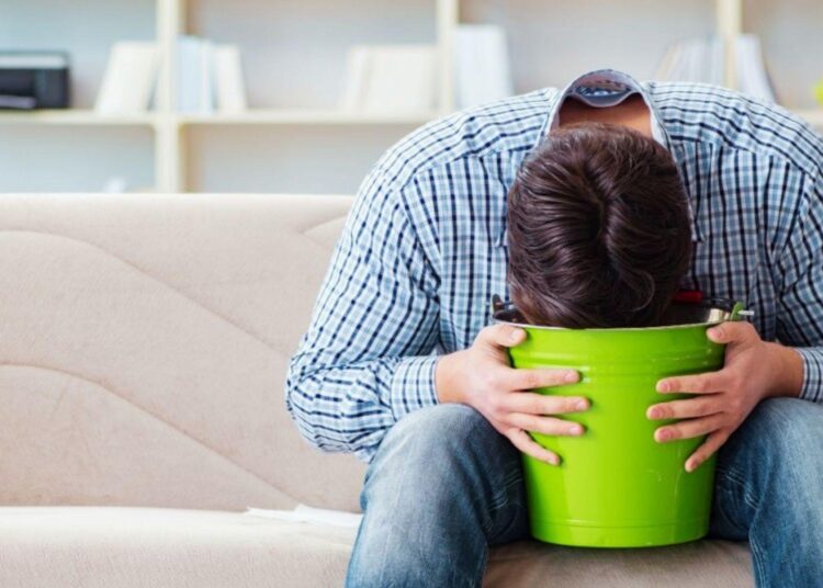 Man feeling nauseous and vomiting into green bucket as a common weed hangover side effect